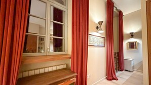 A hallway with red curtains, a wooden bench, a radiator, and a framed picture on the wall.