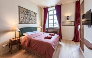 A bedroom with a bed, bedside lamps, a desk, a window with curtains, a painting on the wall, and a flat-screen TV. - 1 bedroom amazing apartment in Juilly (Juilly)