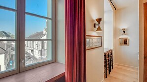 A room with a large window, a red curtain, a staircase, and wall-mounted lighting fixtures.