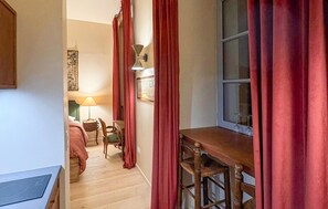 Un couloir étroit avec un lit, une chaise, une table et une fenêtre avec des rideaux.