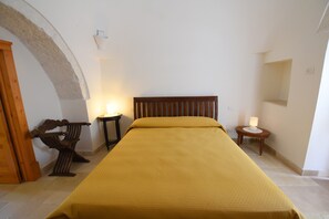Un dormitorio con una cama, una mesita de noche, una lámpara y un banco de madera.