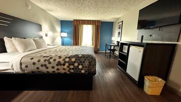 A hotel room with a bed, desk, chair, TV, and a trash bin.