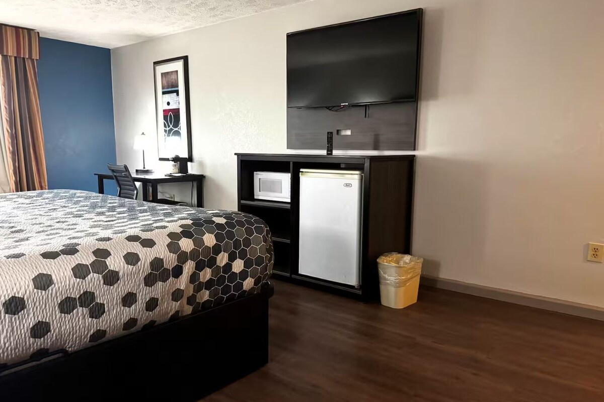 Habitación de hotel con cama, escritorio con computadora, televisión y basurero.