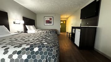 A hotel room with a large bed, a desk, a television, and a refrigerator.