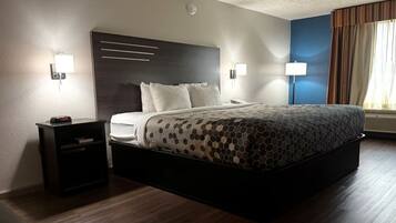 A hotel room with a large bed, bedside tables, a wall-mounted clock, and a window with curtains.