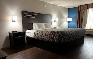 Habitación de hotel con una cama grande, mesitas de noche, un reloj en la pared y una ventana con cortinas.