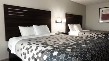 A hotel room with two beds, a dark headboard, a nightstand with a phone, and a wall-mounted light fixture.