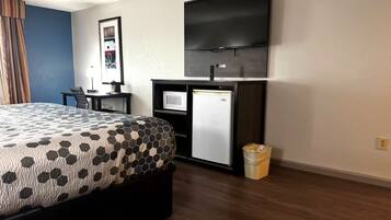 A hotel room with a bed, a desk with a computer, a television, and a trash bin.