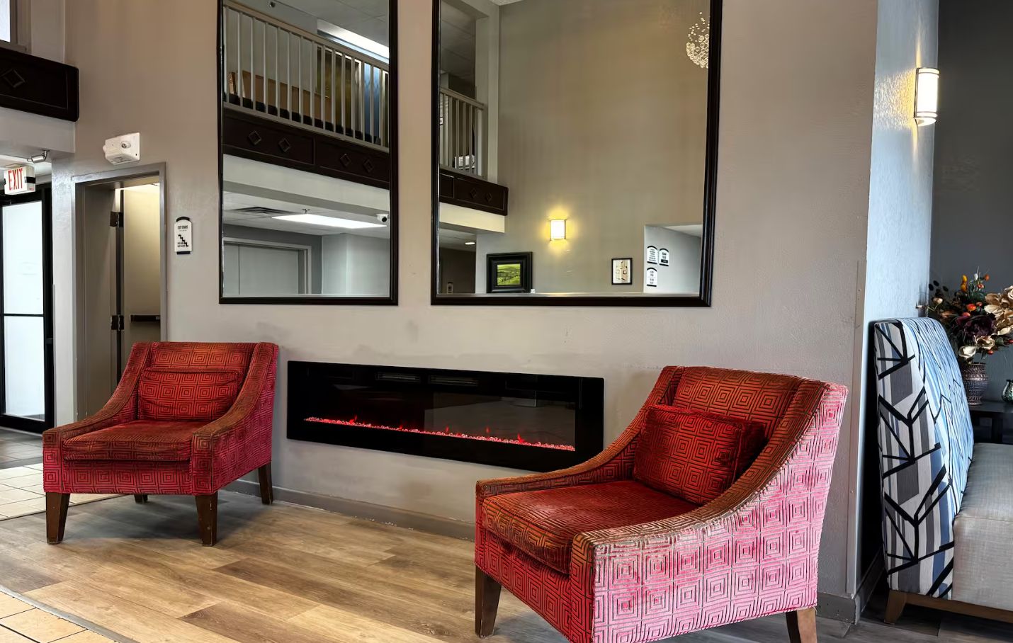 A lobby with two patterned armchairs, a fireplace, and a large mirror.