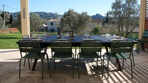 Un espace extérieur aménagé pour les repas, avec une table dressée pour six personnes, entourée de chaises vertes, et offrant une vue sur les arbres et les montagnes en arrière-plan.
