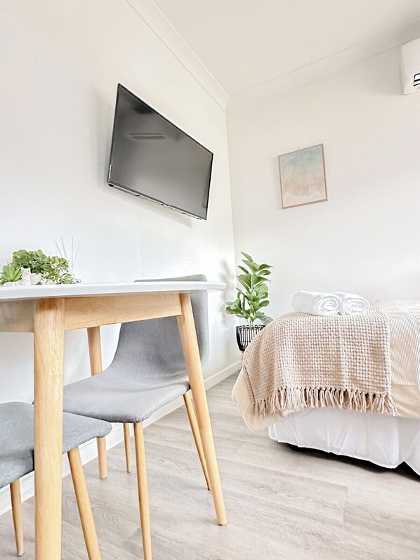 Une chambre moderne comprenant un lit, un bureau avec une chaise, un téléviseur fixé au mur et une petite plante.