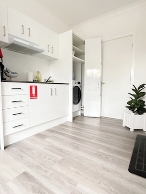 Une cuisine moderne avec des meubles blancs, un lave-linge encastré et un extincteur.