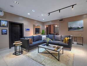 A modern living room with a sectional sofa, a coffee table, a small side table, and a TV. - Deedee Luxury Apartments (Osogbo)