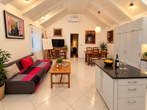 A modern living room with a sofa, a dining table, and a kitchen area with cabinets and a countertop. - House Dalma (Dubrovnik)