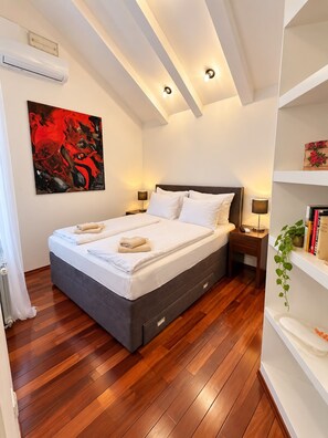 A bedroom with a bed, bedside tables, a wall-mounted air conditioner, a painting, and a bookshelf. - House Dalma (Dubrovnik)