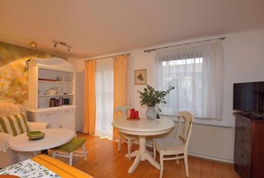 Ein gemütliches Wohnzimmer mit einem Esstisch, Stühlen, einem Bücherregal, einem Fernseher und einem Fenster mit Vorhängen.