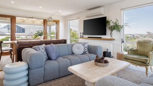 Ein modernes Wohnzimmer mit Sofa, Couchtisch, Fernseher und Blick ins Freie.