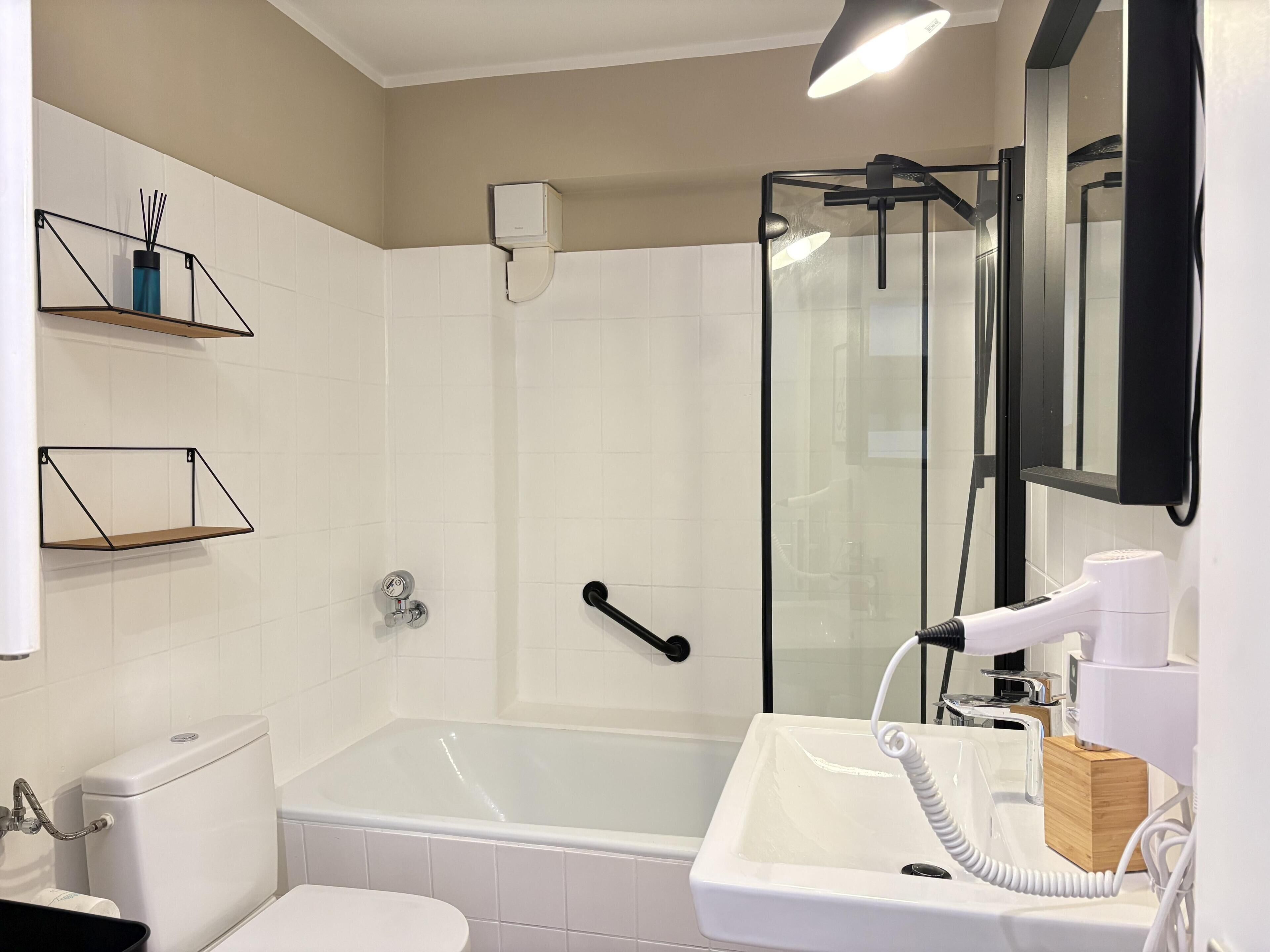 A bathroom with a toilet, sink, shower, and a glass-enclosed shower stall.