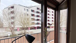 En balkong med ett metallräcke, en vas med blommor och en svart golvlampa.