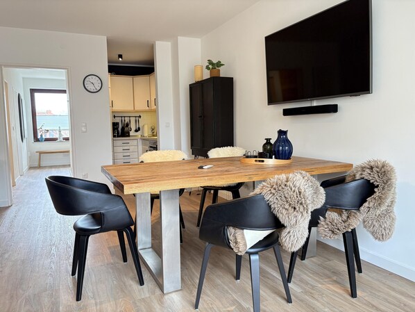 A modern dining area with a wooden table, black chairs, and a television mounted on the wall.