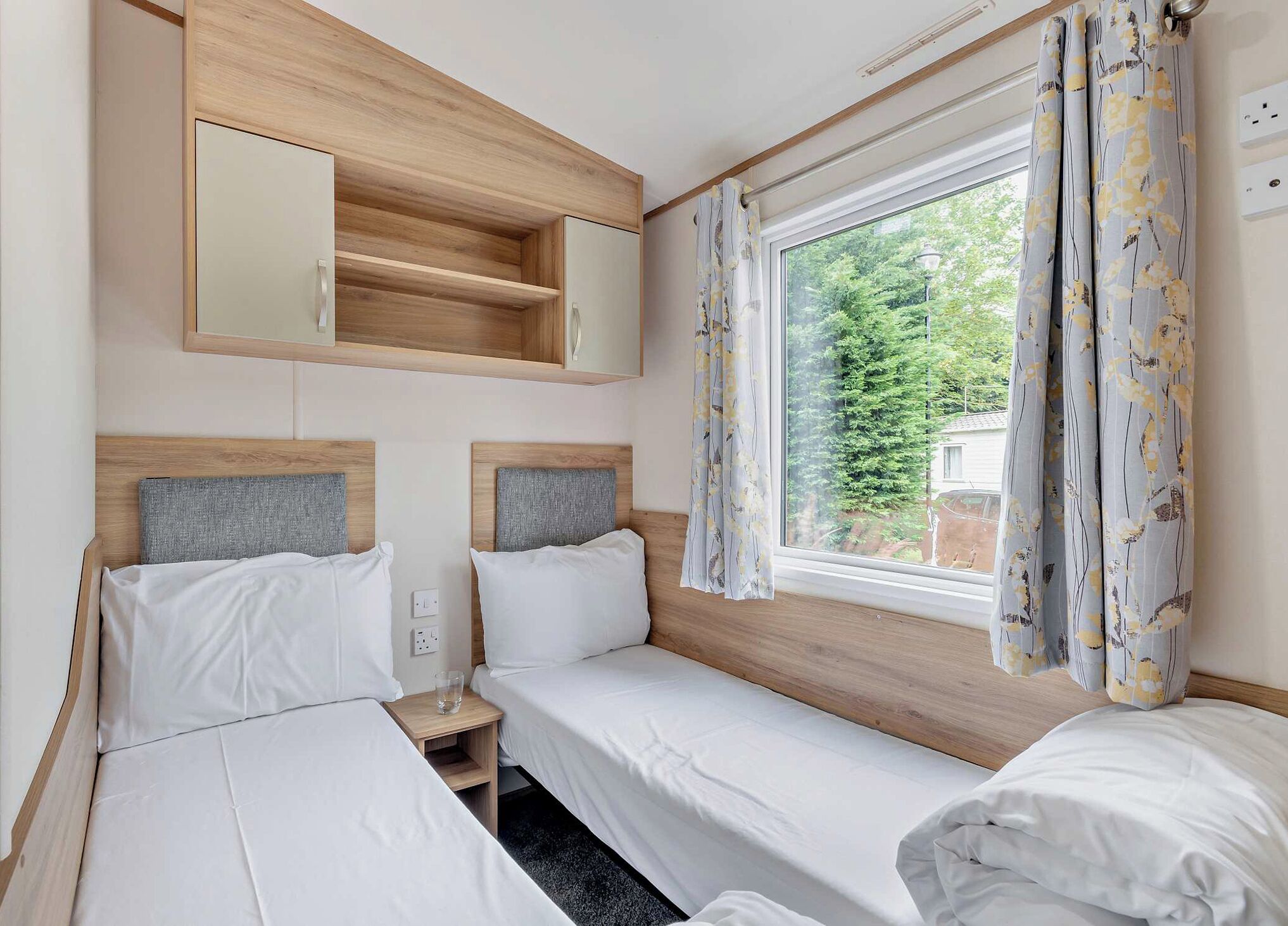 A double bed room with a wooden headboard, a bedside table, a mirror, and a window with curtains.