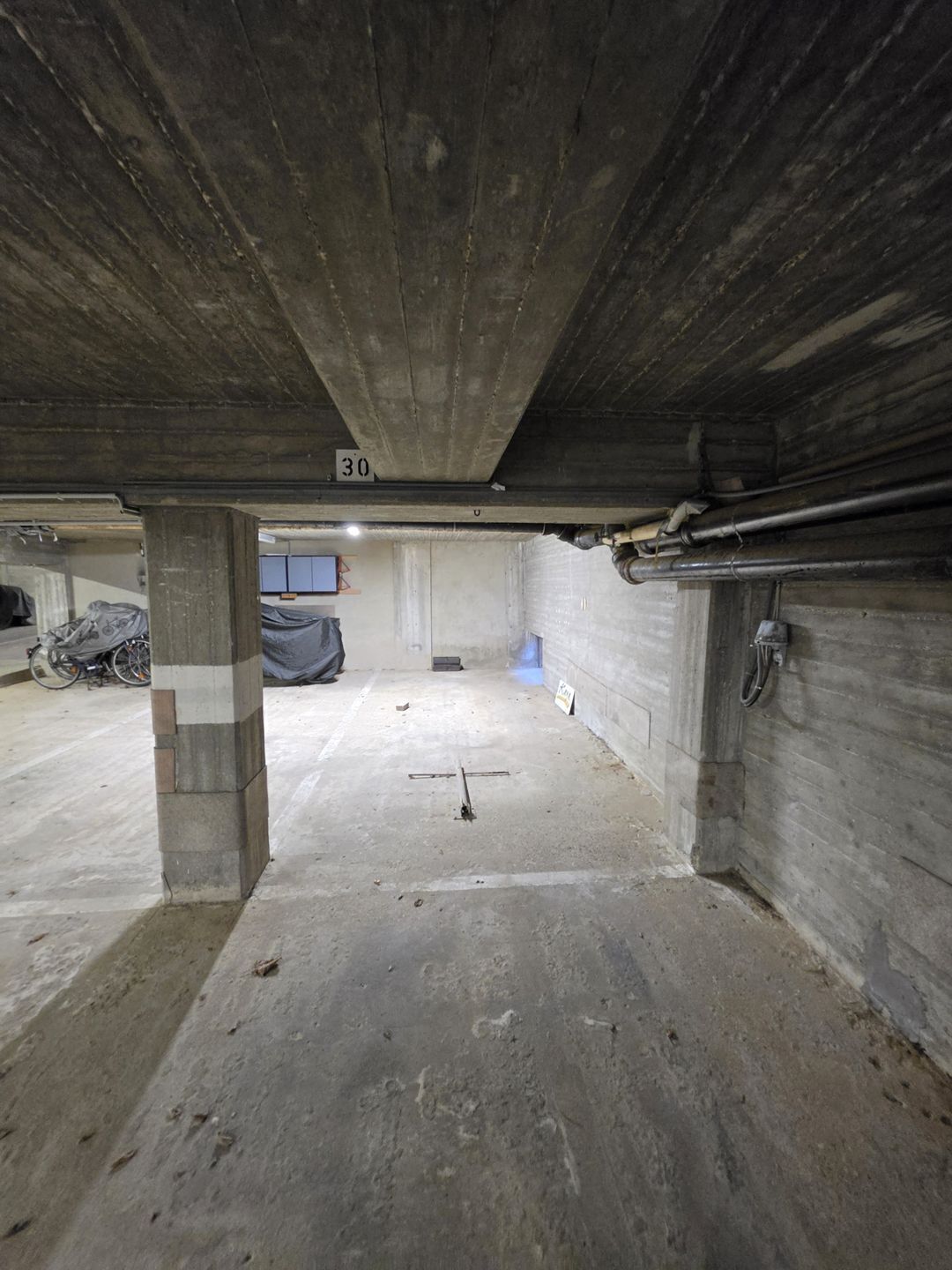 Eine Tiefgarage mit Betonsäulen, einer sichtbaren Nummer 30 und einem blauen Schild an der Wand.