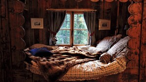 Ein rustikales Zimmer mit Holzboden, einem großen Bett, einem Fenster mit Vorhängen und gerahmten Bildern an den Wänden.