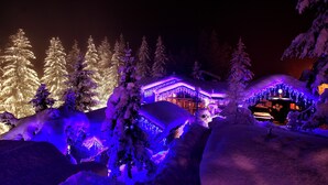 Schneebedeckte Landschaft mit beleuchteten Bäumen und einem Gebäude mit warmem Schein.