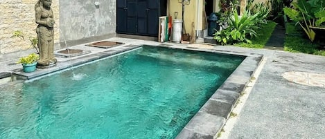 A rectangular swimming pool with clear water, surrounded by a stone border, and a statue on the left.