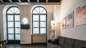 Een kamer met een bank, twee rondboogvensters, een radiator en kunstwerken aan de muur.