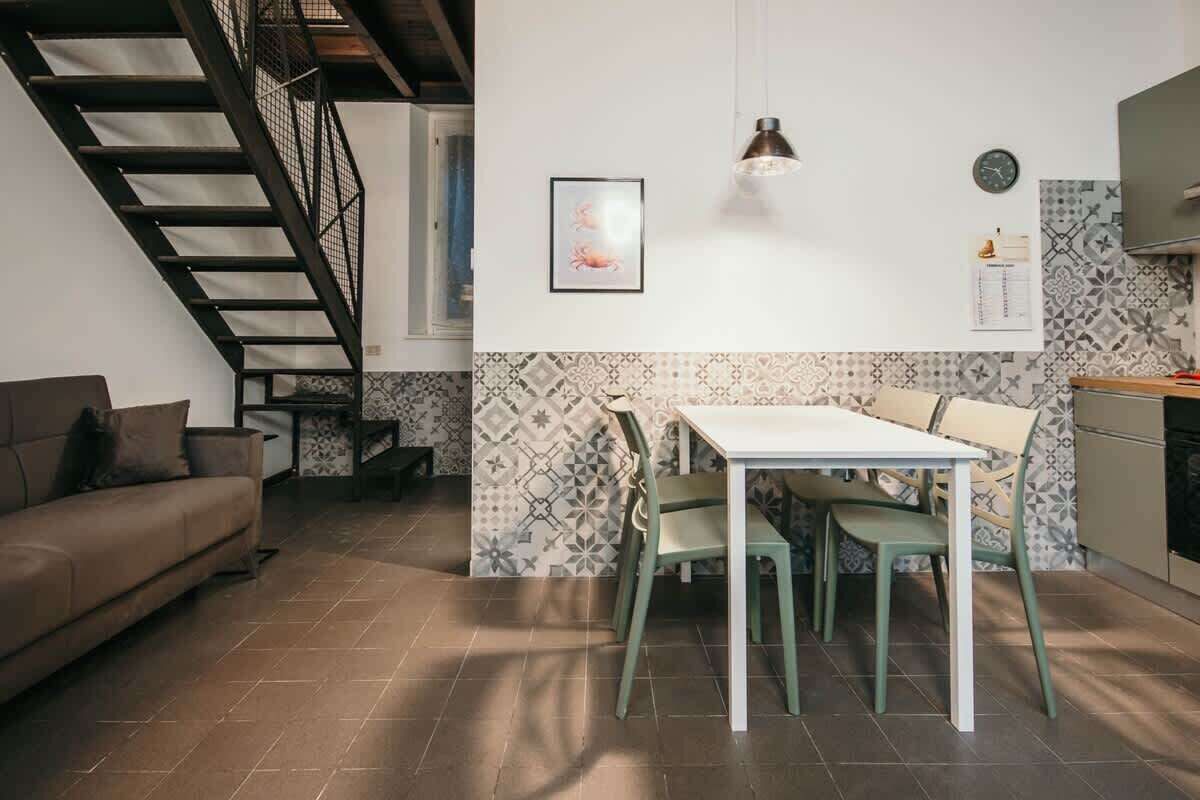 A modern kitchen with a dining area, a staircase, and a living room with a sofa.