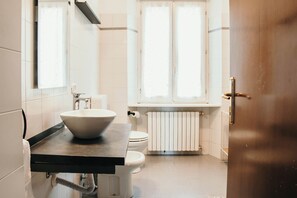 A bathroom with a large vessel sink, a toilet, and a window with curtains. - Bigattera Ciliegio - Lakeside L&B (Varese)