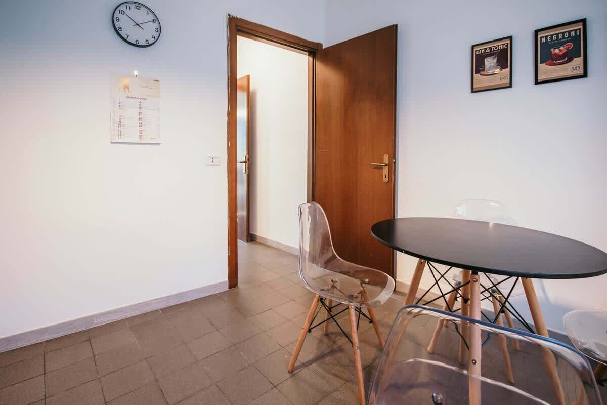 A room with a wooden door, a wall clock, a calendar, a clear chair, and a round table.