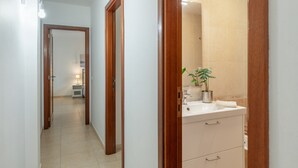 Un couloir menant à une salle de bain équipée d’un lavabo, d’un miroir et d’une plante en pot.