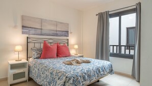 Une chambre à coucher avec un lit, deux tables de chevet avec des lampes, une fenêtre avec des rideaux et un tableau au mur.