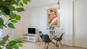 Un espace repas moderne avec une table en verre, des chaises noires, un meuble blanc et un téléviseur à écran plat.