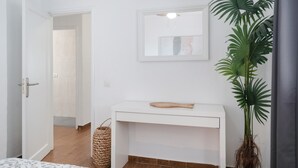 Ett rum med ett vitt konsolbord, en krukväxt, en flätad korg och en dörr som leder till ett annat rum.