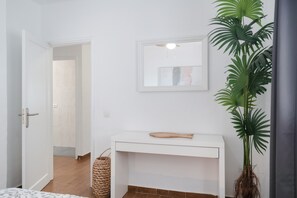 Ein Zimmer mit einer weißen Kommode, einem Topf mit Pflanze, einem gewebten Korb und einer Tür zu einem anderen Raum.