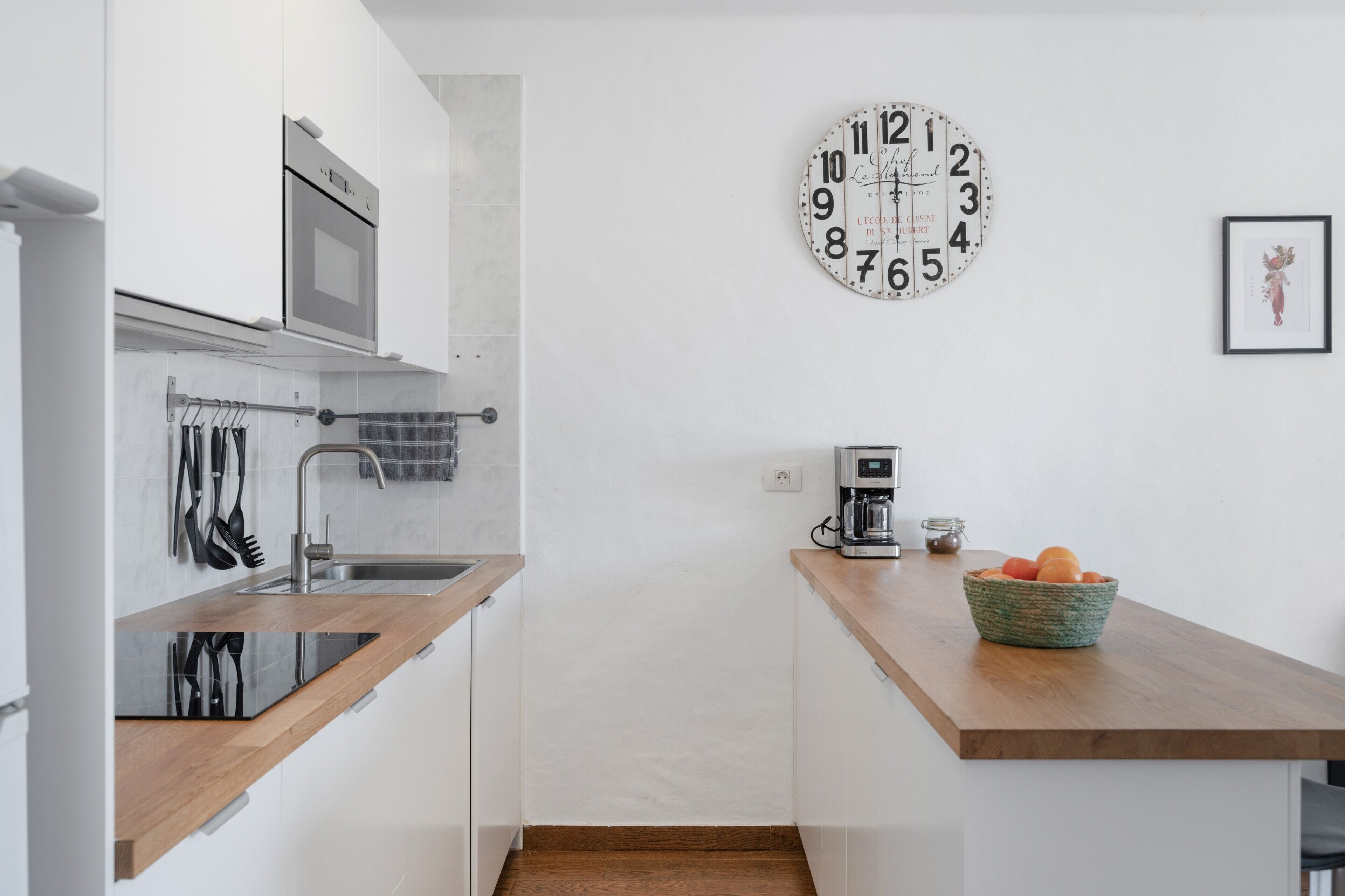 A modern kitchen with a built-in oven, a coffee maker, and a clock on the wall.