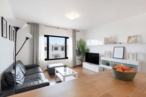 A modern living room with a leather sofa, a coffee table, a TV, and a basket of oranges. - Apartment with Spacious Terrace by the Beach (Tías)
