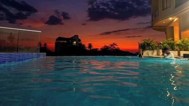 A swimming pool with a sunset view, a building with balconies, and a distant house. - Ocean view + Direct beach view in Pozos colorados (Urb Plenomar)