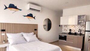 A modern bedroom with a large bed, a round mirror, and a kitchen area with cabinets and a refrigerator. - Ocean view + Direct beach view in Pozos colorados (Urb Plenomar)