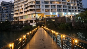 A multi-story hotel with a curved facade, a wooden boardwalk leading to the entrance, and a river in the foreground. - Ocean view + Direct beach view in Pozos colorados (Urb Plenomar)