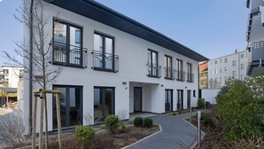 Un bâtiment moderne à deux étages, doté de balcons, d’une allée pavée et d’un petit jardin.