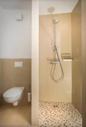 Une salle de bain comprenant des toilettes, une douche avec un pommeau de douche amovible et un sol carrelé.