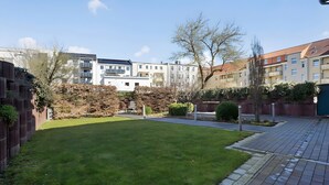 Un quartier résidentiel avec une pelouse bien entretenue, un chemin piétonnier dallé et, au fond, des immeubles à plusieurs étages.