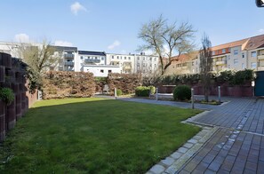 Ein Wohngebiet mit einem gepflegten Rasen, einem gepflasterten Weg und mehrstöckigen Gebäuden im Hintergrund.