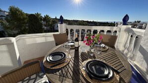 A round table with a bottle of wine, glasses, and a vase with flowers on a balcony overlooking a scenic view. - Rabat 23 in Oasis de Capistrano Nerja (Nerja)