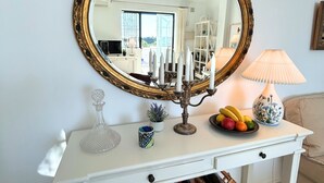 A white console table with a gold-framed mirror, a candelabra, a fruit bowl, a wine rack, and a potted plant. - Rabat 23 in Oasis de Capistrano Nerja (Nerja)
