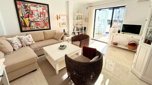 A living room with a sofa, coffee table, wicker chair, TV, and a large window. - Rabat 23 in Oasis de Capistrano Nerja (Nerja)